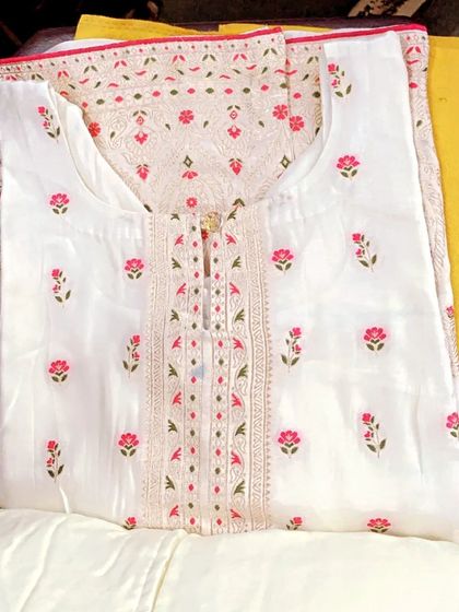 A classic white suit with delicate pink and green floral embroidery. The detailed work on the neckline makes it an elegant choice for daytime events.