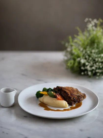 A refined and delicate main course. Our Braised and Pulled Lamb Crumbed Steak features a caramelized onion and mint crust, served with creamy mashed potatoes and a savory lamb jus.