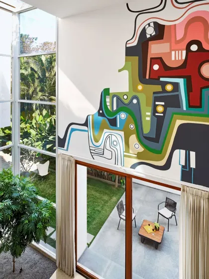 A vibrant, custom mural brings a layer of art and personality to the minimalist interior of the Split House. Viewed from the connecting bridge, this double-height wall becomes a canvas that overlooks the living area and garden, showcasing our collaborative approach to integrating art directly into the architectural fabric of a home.