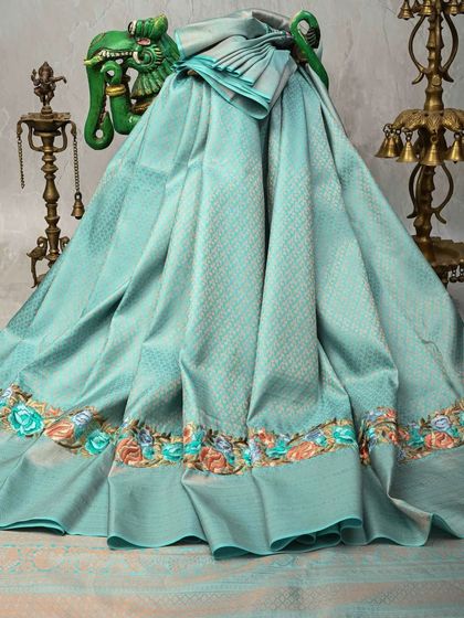 A pastel blue Kanjivaram silk saree with a delicate floral embroidered border. This piece is perfect for those who love subtle elegance and fine craftsmanship.