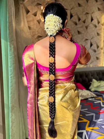 A classic South Indian bridal hairstyle, featuring a long, thick braid decorated with fresh jasmine flowers (gajra) and traditional gold ornaments.