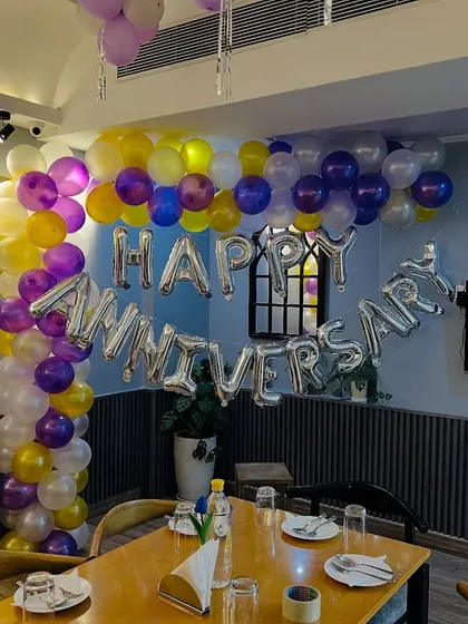 An anniversary celebration setup in a restaurant. I used a colorful balloon arch with purple, yellow, and white balloons, along with silver foil "Happy Anniversary" letters to decorate the space.