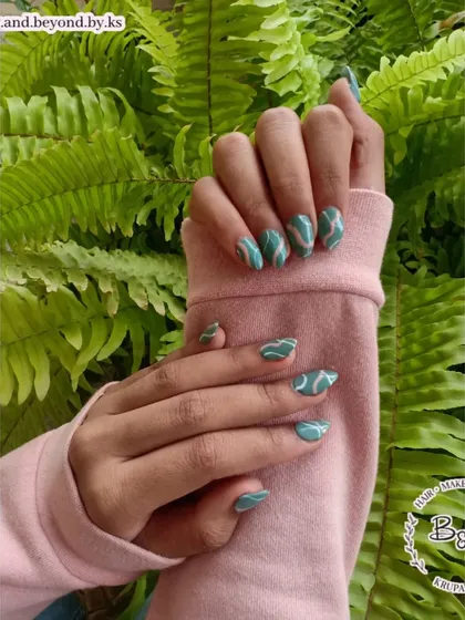 I love playing with trendy and abstract designs like these swirl nails. This look features freehand white swirls over a beautiful teal base on short almond extensions, set against a natural background that makes the color pop.
