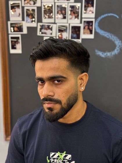 The front view of a sharp haircut, showing how the taper fade frames the face and complements the styled top and shaped beard.