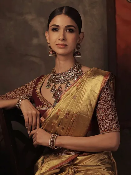 A model wearing a deep red blouse with intricate floral embroidery, paired with a stunning gold Kanchipuram saree. This is a classic and opulent combination for any bride.