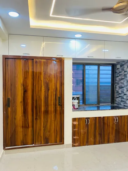 A bedroom featuring a sliding wardrobe with a rich, glossy wood finish, paired with a matching window seating area and storage cabinets.