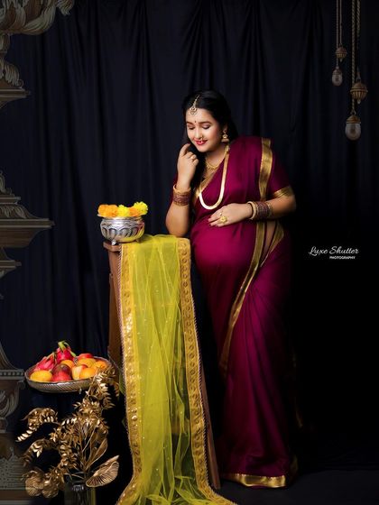 A beautiful composition with rich colors and textures. The deep black curtain, golden props, and vibrant saree create a luxurious and traditional setting.