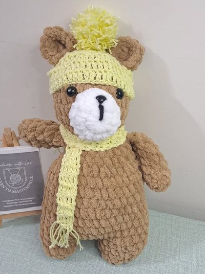 A plush teddy bear wearing a yellow pom-pom hat and scarf.