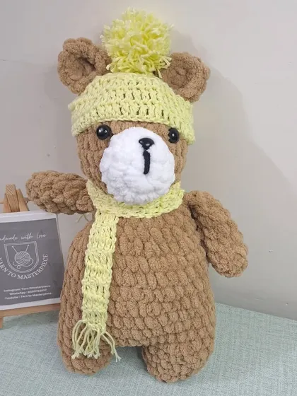 A plush teddy bear wearing a yellow pom-pom hat and scarf.