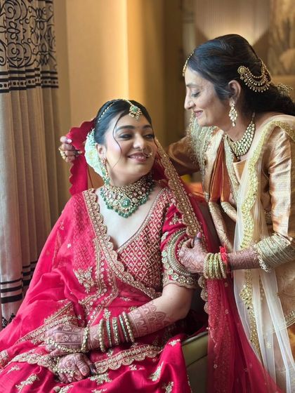 A touching moment between the bride and her mother. Her smile reflects the joy and confidence she feels in her final look, a beautiful red lehenga complemented by emerald jewelry.