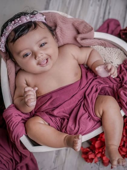 A cheeky little grin. This awake baby, nestled in a heart-shaped bowl, looks so sweet against the rich magenta and red floral background.