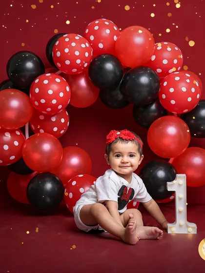 A Minnie Mouse inspired first birthday shoot. The bold red backdrop, polka-dot balloons, and a light-up number '1' create a classic and cheerful setting for this milestone.
