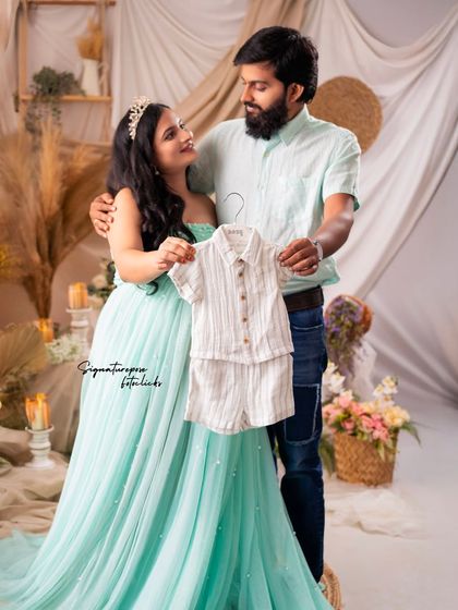 A creative announcement shot! The couple holds up a tiny outfit, dreaming of their baby's arrival.