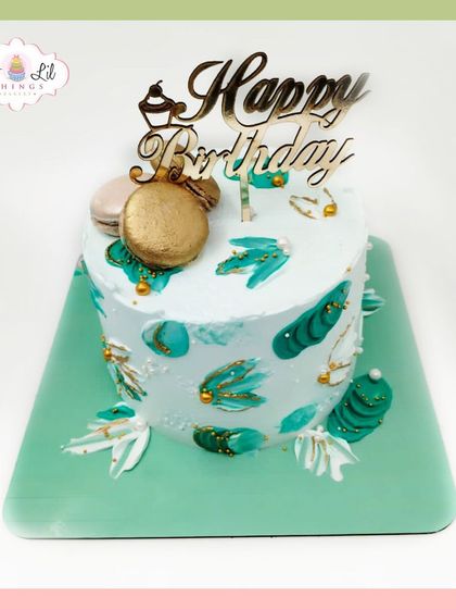 An elegant birthday cake with a teal and gold color scheme, decorated with macarons and abstract brushstrokes.