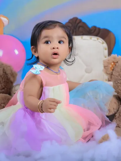A close-up shot capturing the birthday girl's curious expression. The soft pastel colors of her dress perfectly match the rainbow theme.