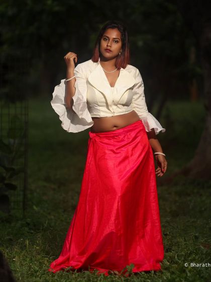 A fashion-forward portrait in a park setting. The contrast between the bright red skirt and the dark green background is striking.