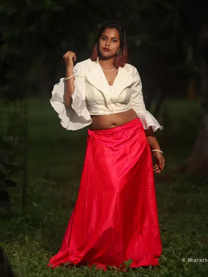 A fusion outfit featuring a white crop top with dramatic ruffled sleeves and a vibrant pink skirt. The outdoor park setting adds a soft, natural light to the shot.