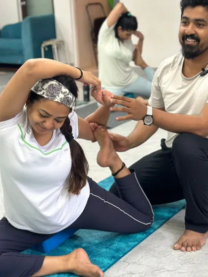 A teacher provides a gentle, encouraging assist to a student in a hip-opening pose, helping her find more space and comfort in the stretch.