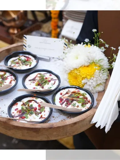 A server presents a tray of our Dahi Bhalla cups. The individual portions, wooden spoons, and floral garnish make for an elegant and convenient way to serve this classic chaat.