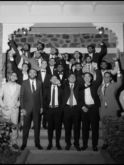 A black and white group photo of the groom and his groomsmen cheering together, full of energy and camaraderie.