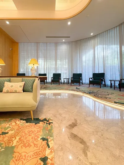 A wide shot of the curved seating area in the GCC Hotel lobby. The design uses natural light from the large windows to illuminate the polished marble floors and the rich textures of the furnishings.