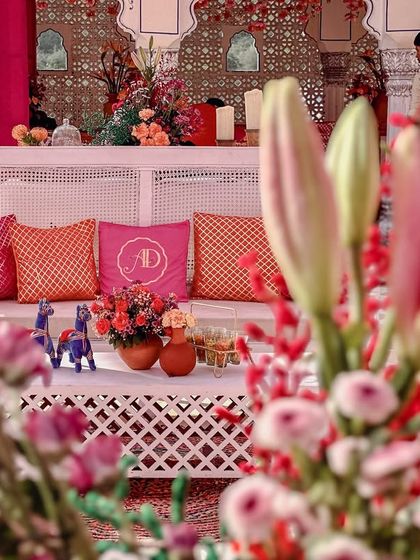 For the lounges at the Mehendi, we used white furniture to balance the vibrant pink and orange decor. The custom cushions with the couple's initials added a lovely, personalized touch.