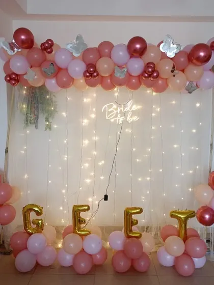 This bridal shower decoration features a balloon garland over a backdrop of sheer curtains and fairy lights. The "Bride to be" neon sign adds a modern glow, and I can spell out names or words with foil balloons, as seen here.
