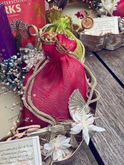 A detail of a vibrant pink potli with gota patti work, part of a larger Diwali arrangement. The mix of textures, from the soft fabric to the delicate dried flowers, creates a rich sensory experience.