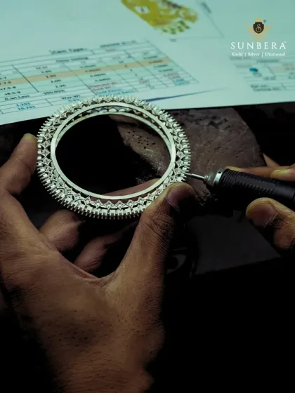 A close-up view of the polishing process. You can see the artisan's steady hand as they work on a diamond bangle, with the detailed design sheet visible in the background. This is precision work that requires immense focus.