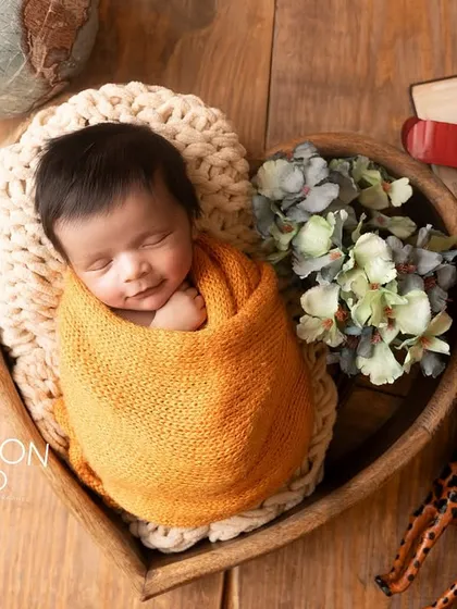 A newborn sleeps soundly in a heart-shaped wooden bowl, wrapped in a warm ochre swaddle. The travel-themed props hint at the great adventures to come.
