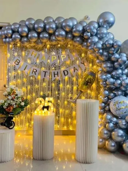 A glamorous silver-themed 25th birthday decoration with a full sequin wall, fairy lights, and a metallic silver balloon garland.