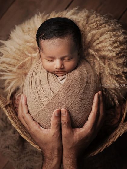 Of all the things my hands have held, the best by far is you. This powerful shot shows a father's hands securely holding his swaddled newborn in a basket, a symbol of protection and love.