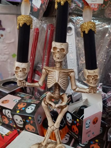 A spooky skeleton candelabra. This detailed decoration features a skeleton holding three black candles, perfect for creating a haunted mansion vibe on your party table.