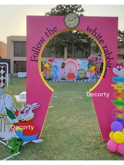 "Follow the white rabbit" through this fun entrance arch into a whimsical Wonderland party. The setup is complete with character cutouts and playful signs.