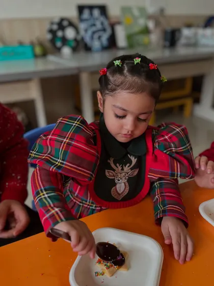 A close-up of a girl decorating her cookie with chocolate and sprinkles.