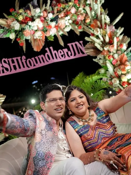 The happy couple enjoying their carnival-themed celebration, seated on a beautifully decorated sofa with a custom hashtag sign.