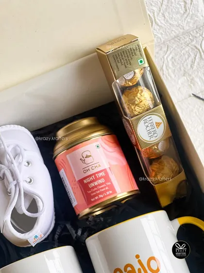 This top-down view showcases the contents of the grandparents' announcement hamper, including the baby shoes, tea, and chocolates.