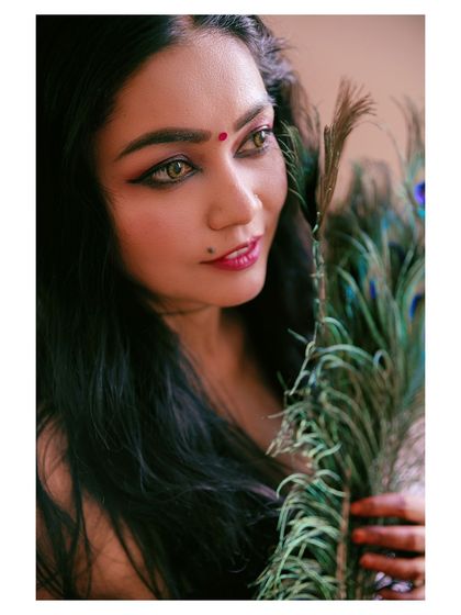 A close-up beauty shot with a focus on the eyes. The peacock feather adds a touch of color and texture, creating an artistic and captivating portrait.