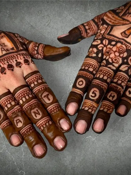 A close-up of the personalized anniversary mehendi, showing the name 'Sant' and the number '05' on the fingers, along with a romantic Punjabi verse on the palm.