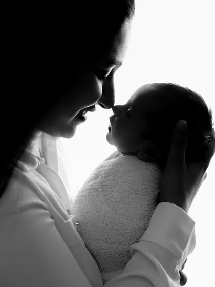An artistic black and white silhouette photo capturing the intimate bond between a mother and her newborn baby, nose to nose.