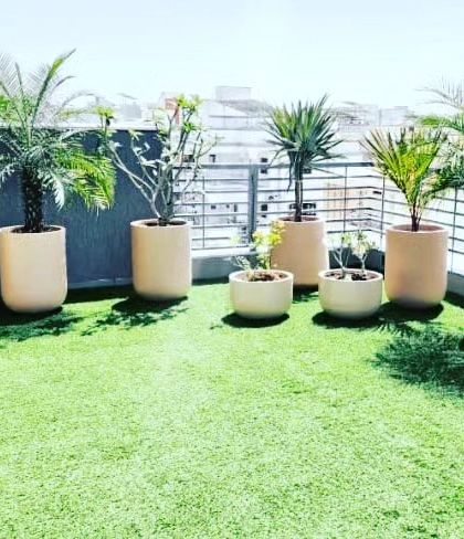 A sunny balcony covered with soft artificial grass, making it a perfect spot for potted plants. This surface does not require watering or mowing and stays green all year.