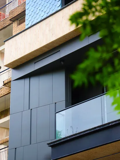 A detail shot showing the contrast between the dark grooved panels, the wood-finish balcony, and the textured shingles. This interplay of materials adds depth and character to the facade.