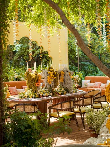A dining table set amidst the lush greenery of the 'Kesar Sehar' Haldi. The centerpiece, made of threaded flowers and candles, added a contemporary touch to the traditional setting.