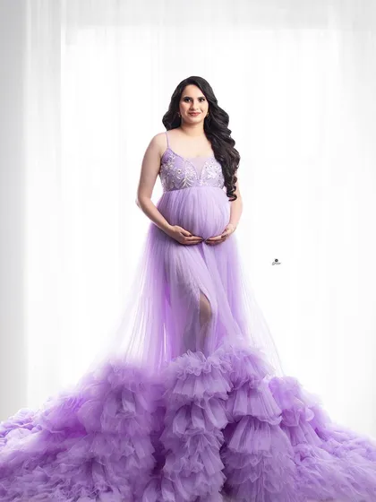 A full-length portrait showcasing a stunning lavender gown with a long, ruffled train. The clean, bright background makes the beautiful color and texture of the dress stand out.