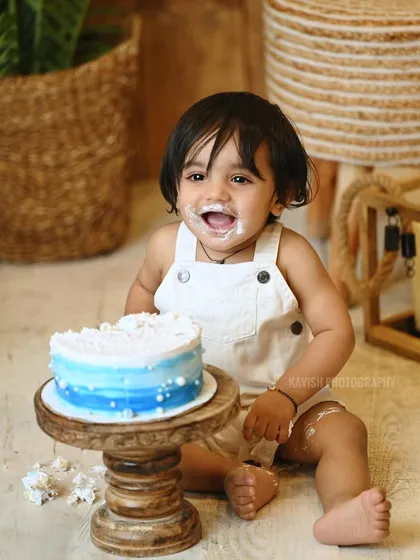 A classic 'cake smash' photo, capturing the baby's joyful and messy exploration of his first birthday cake.