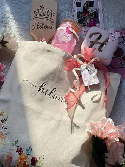A personalized tote bag filled with goodies for a bridesmaid. This one includes a custom hairbrush, a monogrammed jewelry box, and an "I Do Crew" tumbler, making it a beautiful and practical gift.