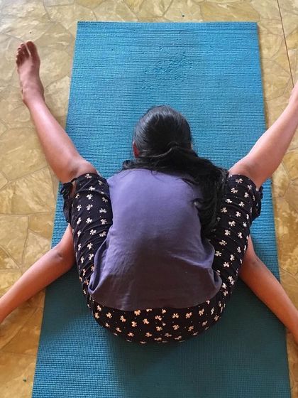 A young student demonstrates Kurmasana (Tortoise Pose). This deep forward bend opens the hips and shoulders while elongating the spine.