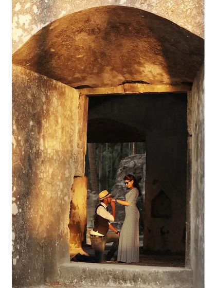 A classic romantic gesture captured in a rustic, historic setting. The man kneels to kiss the woman's hand, creating a vintage, storybook feel for their pre-wedding photoshoot.
