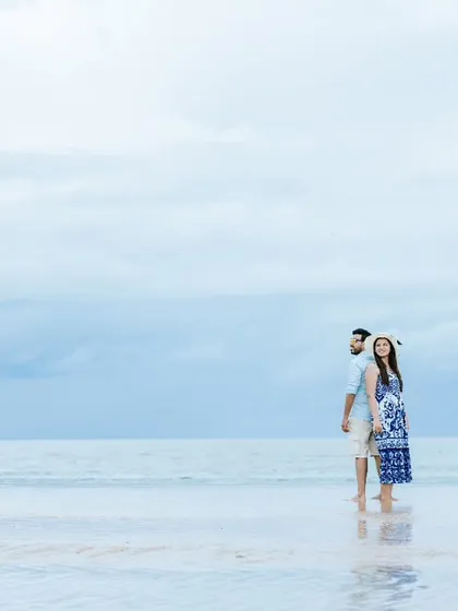 A candid moment as the couple walks along the water's edge. This destination beach photoshoot captures a natural and relaxed interaction between the two.