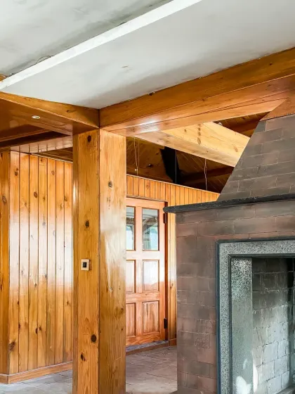 The living area features extensive use of polished wood for walls and structural beams, centered around a large brick and stone fireplace, creating a classic mountain lodge feel.